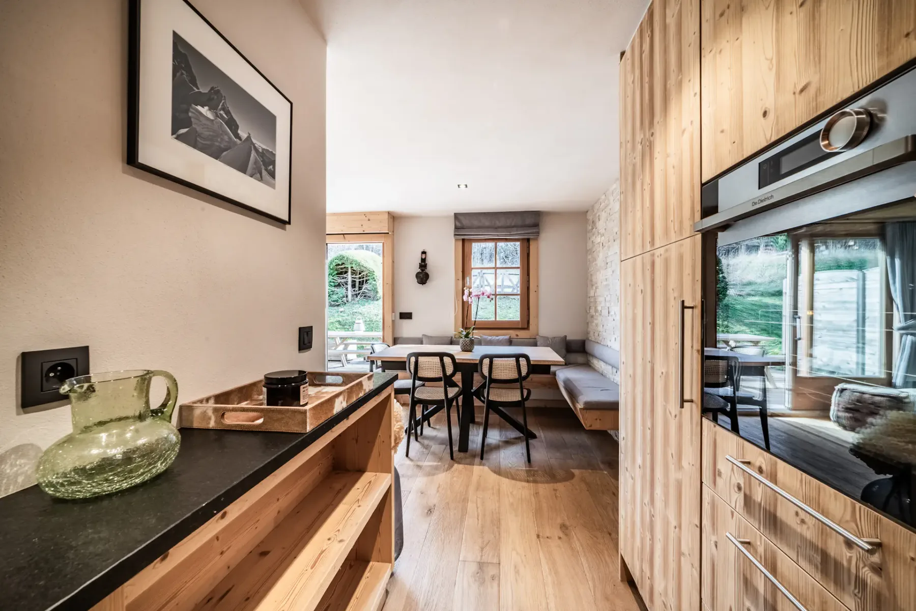 Modern kitchen with wooden cabinets, black countertops, and cozy seating area. Soft lighting and rustic decor create a warm, inviting atmosphere.