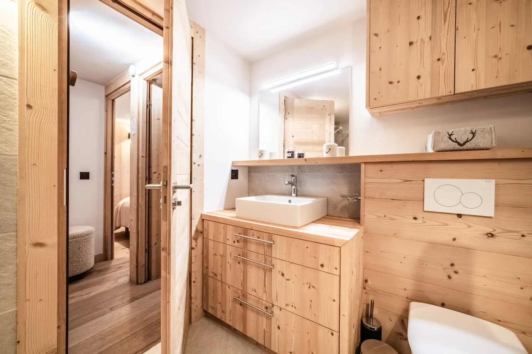 Modern bathroom with wooden accents, featuring a bathtub with glass screen, wall-mounted towel rack, and toilet on a tiled floor.