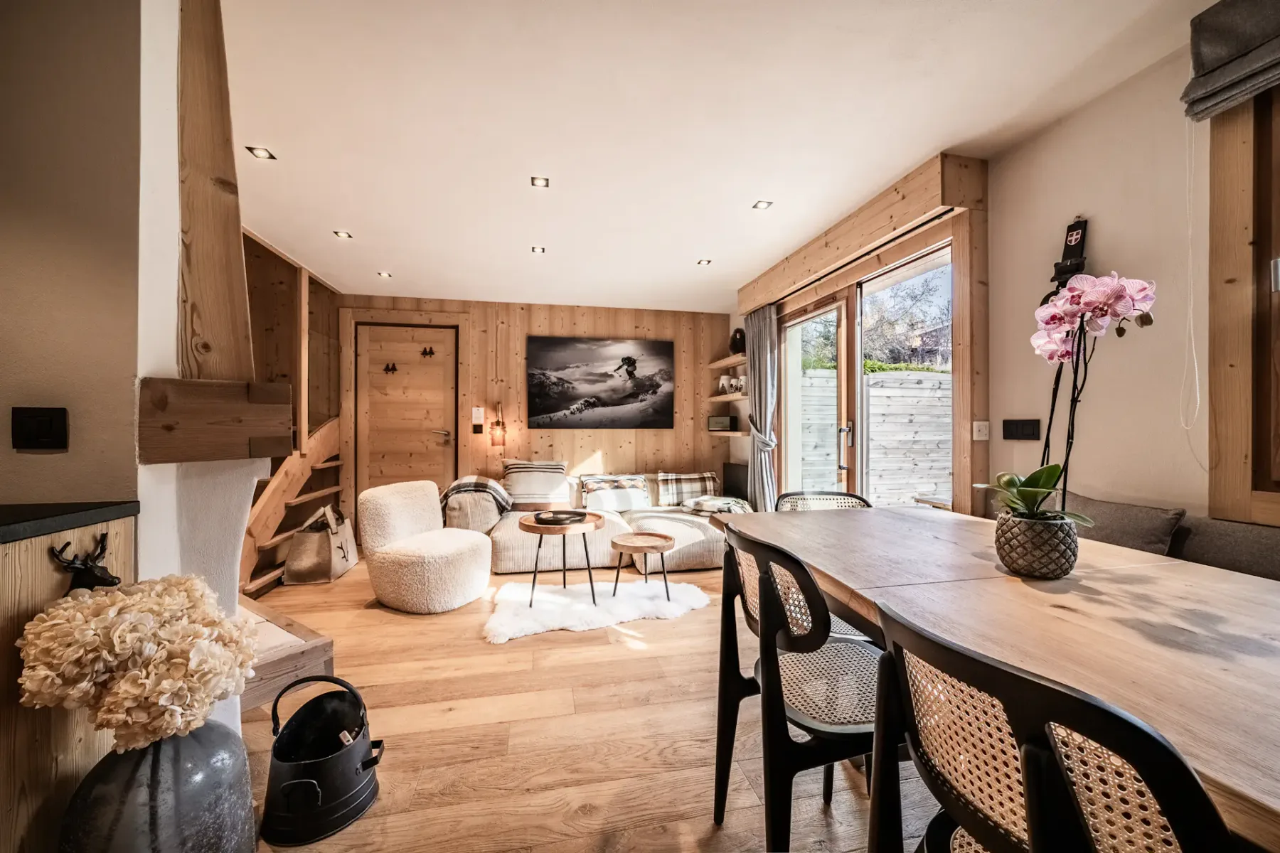 Cozy dining area with a wooden table, chairs, and a corner bench. Stone accent wall, window with a garden view, and a framed picture on the wall.