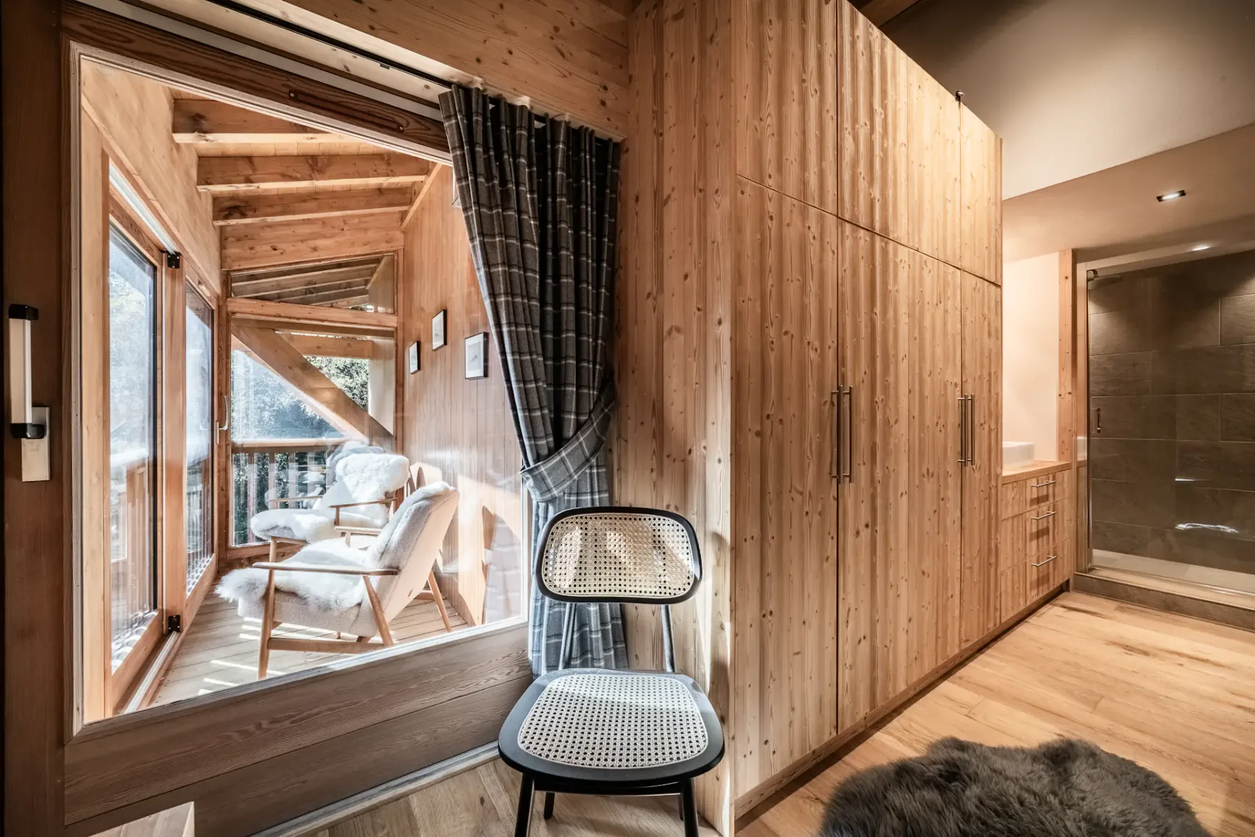 Cozy bedroom with wooden walls, a double bed with white bedding, a painting above the headboard, and a window with plaid curtains.