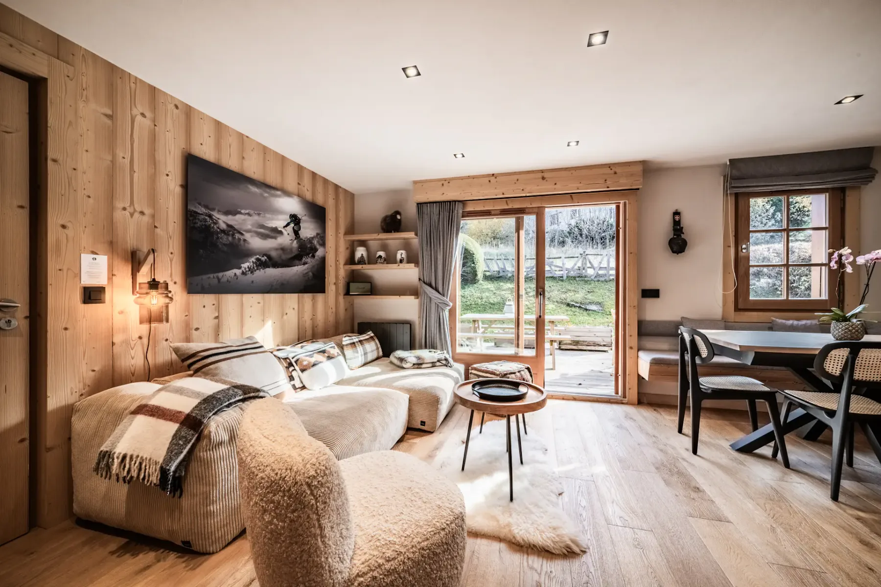 Cozy living room with wooden walls, a staircase, white sofas, a fireplace, and a large photo of a snowboarder on the wall.
