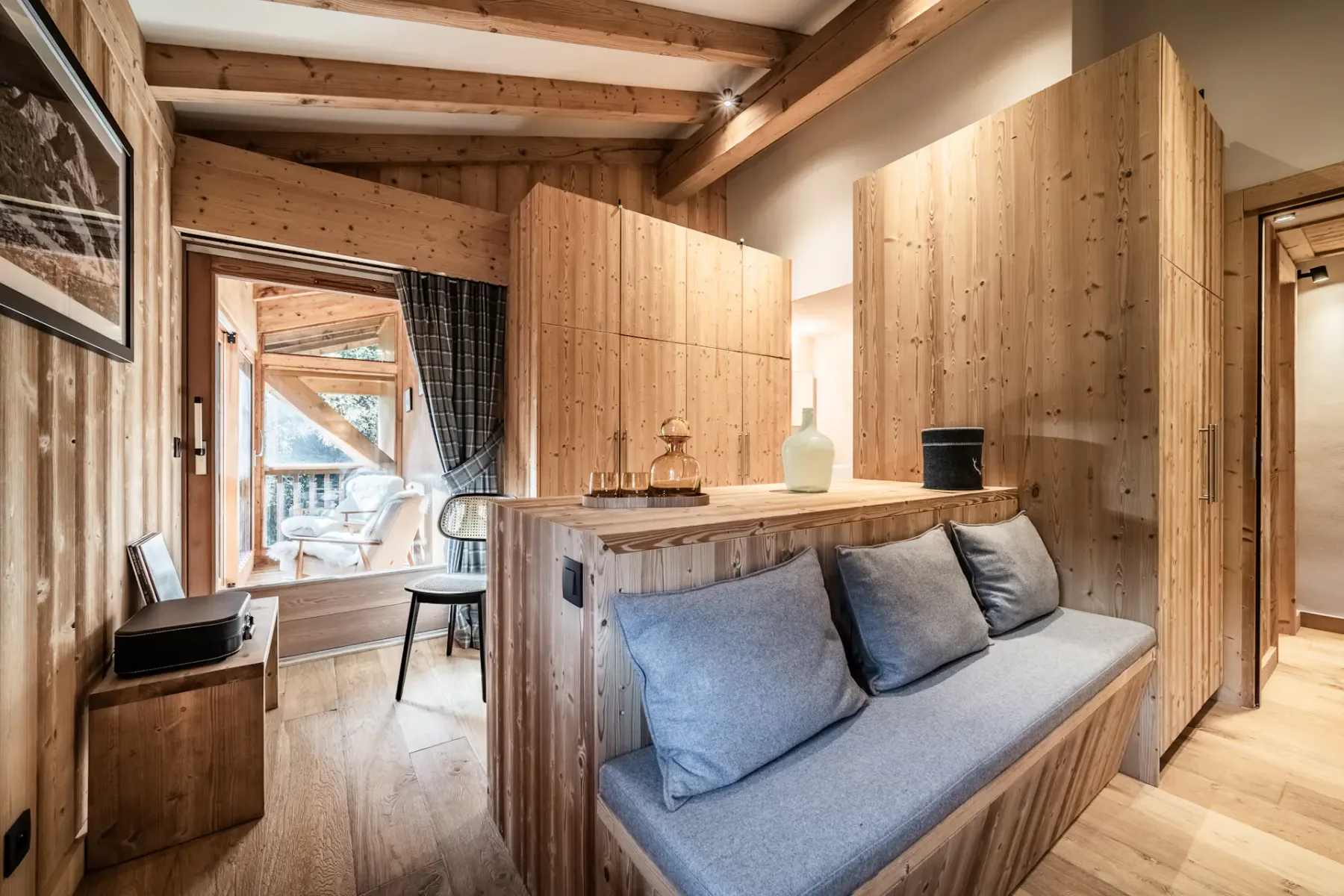 Cozy bedroom with wooden walls, a double bed with white bedding, a painting above the headboard, and a window with plaid curtains.
