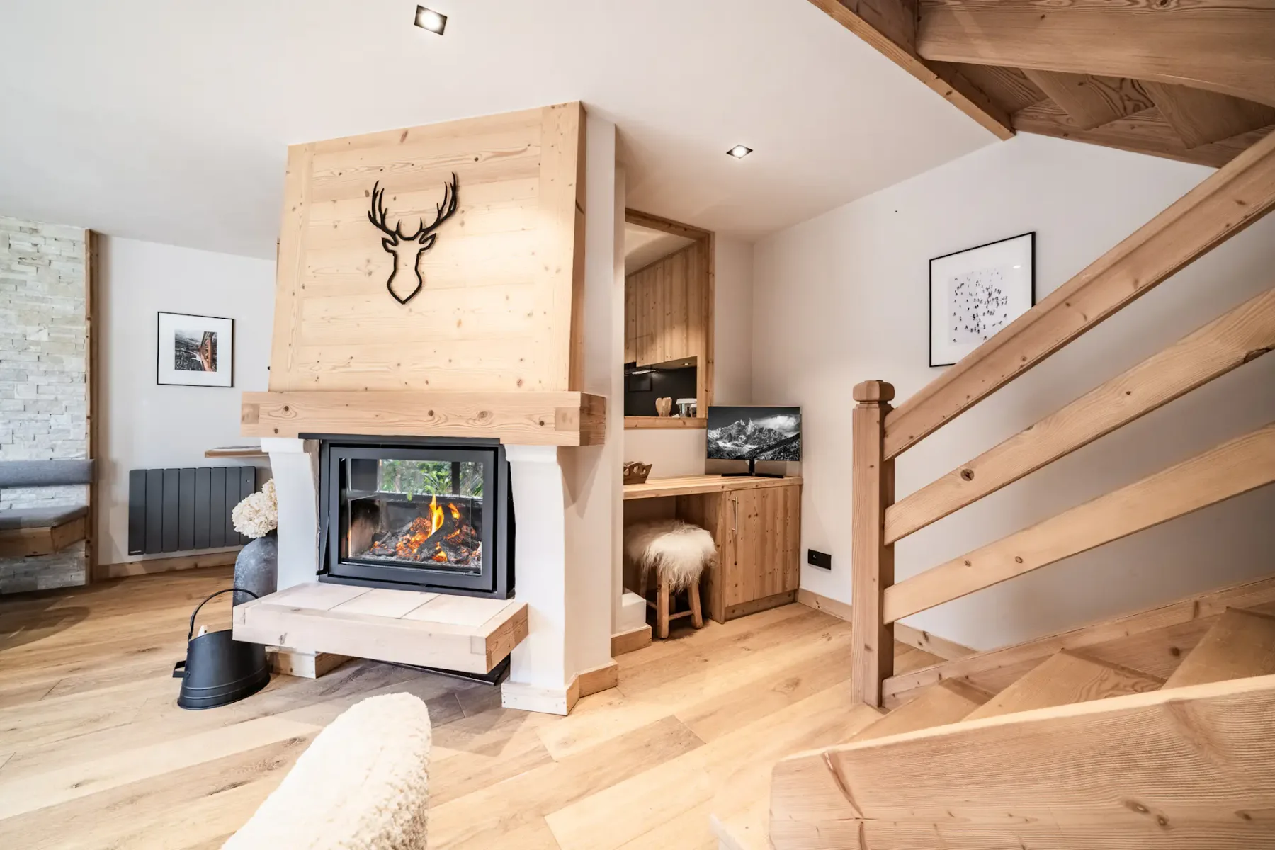 Cozy living room with wooden walls, a staircase, white sofas, a fireplace, and a large photo of a snowboarder on the wall.
