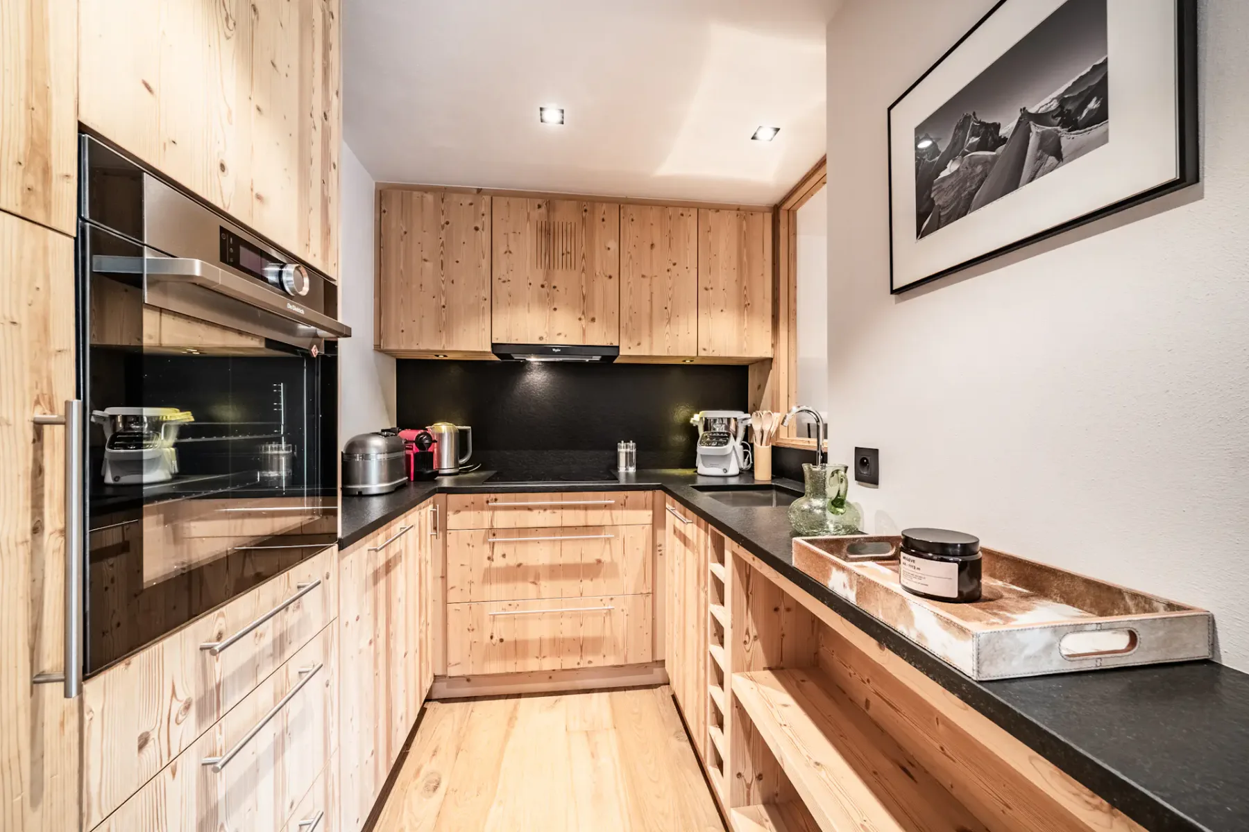 Modern kitchen with wooden cabinets, black countertops, and cozy seating area. Soft lighting and rustic decor create a warm, inviting atmosphere.