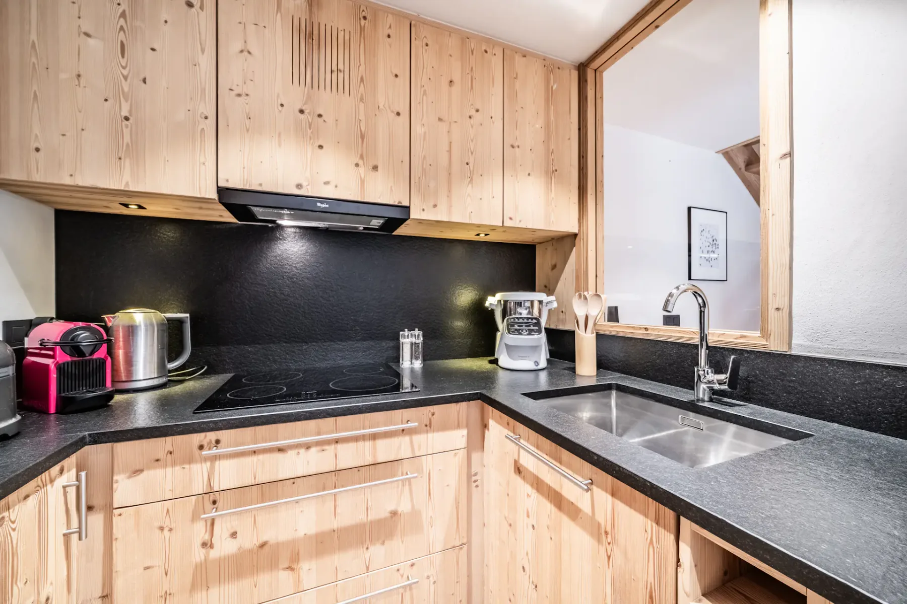 Modern kitchen with wooden cabinets, black countertops, and cozy seating area. Soft lighting and rustic decor create a warm, inviting atmosphere.