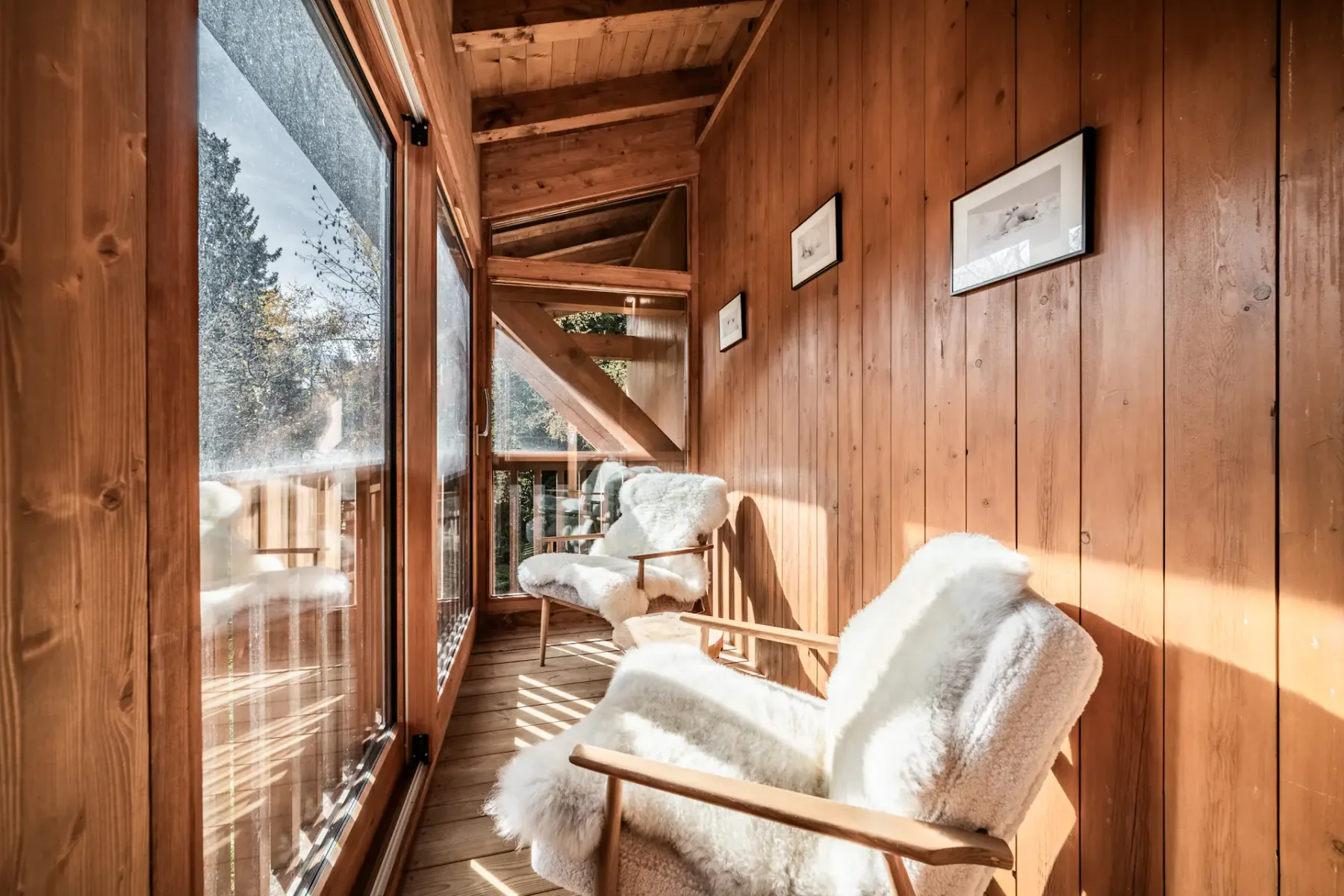 Cozy bedroom with wooden walls, a double bed with white bedding, a painting above the headboard, and a window with plaid curtains.