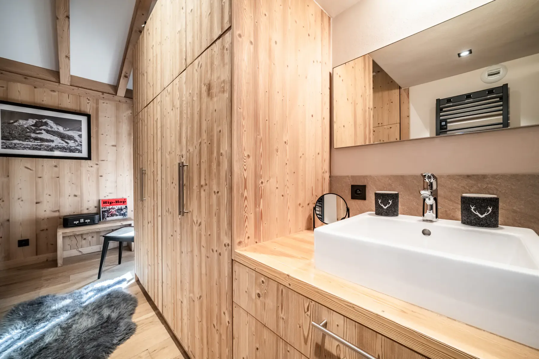 Modern bathroom with a wooden vanity, white rectangular sink, large mirror, glass-enclosed shower, and black towel radiator.