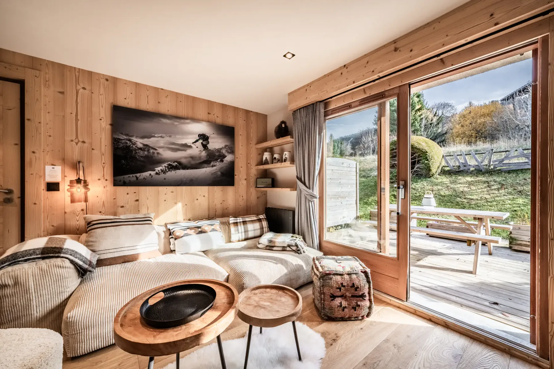 Cozy living room with wooden walls, a staircase, white sofas, a fireplace, and a large photo of a snowboarder on the wall.