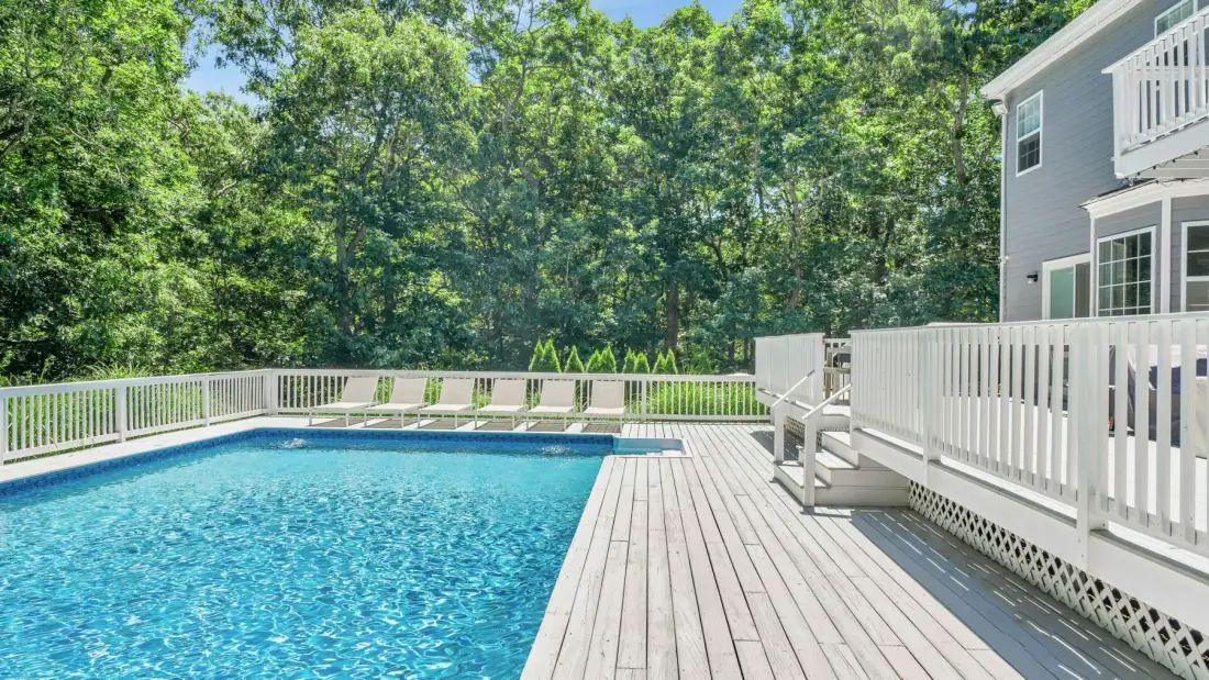 An outdoor swimming pool beside a wooden deck and white railings.