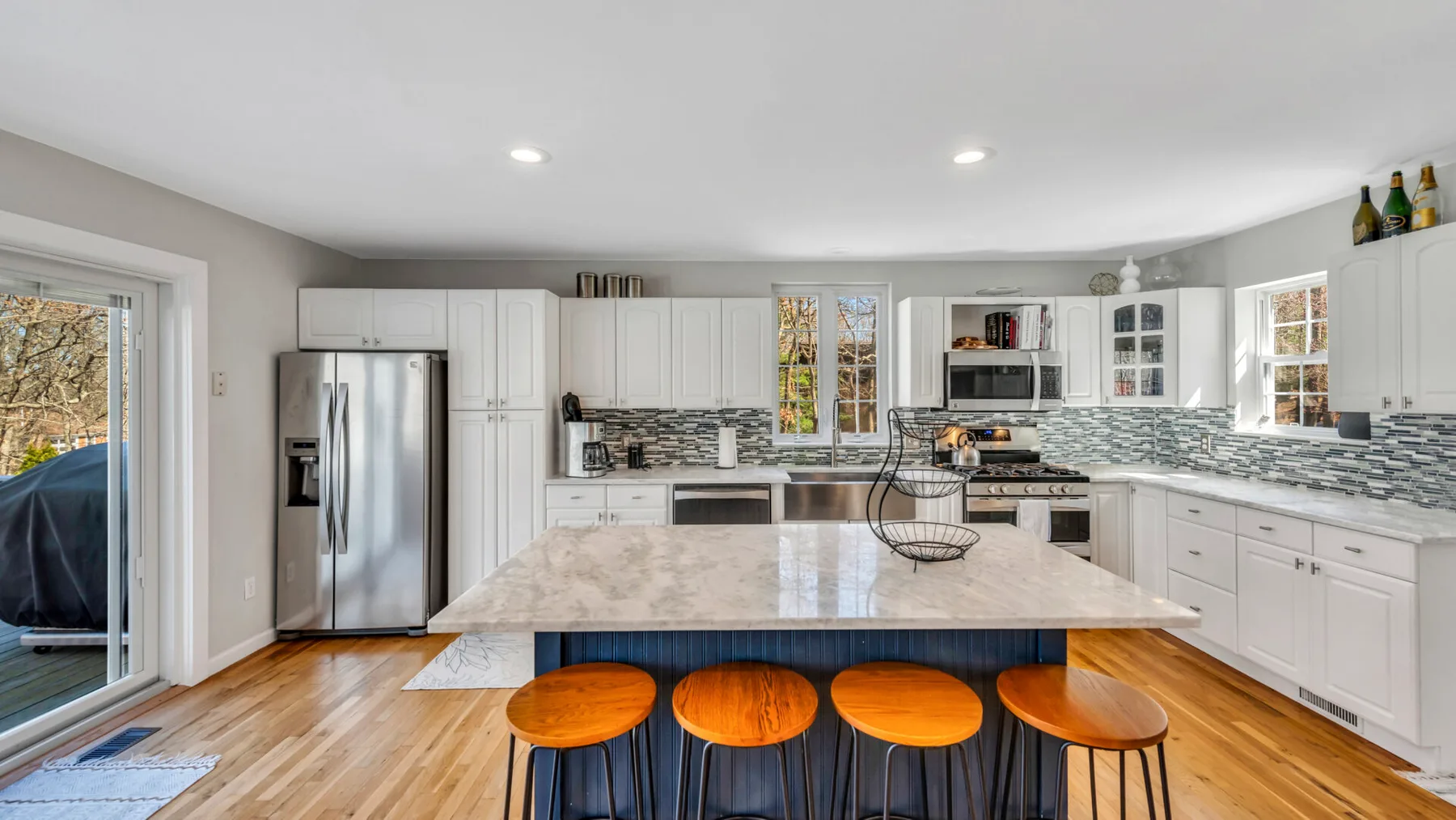 A bright kitchen features white cabinetry, stainless steel appliances, and a large island.