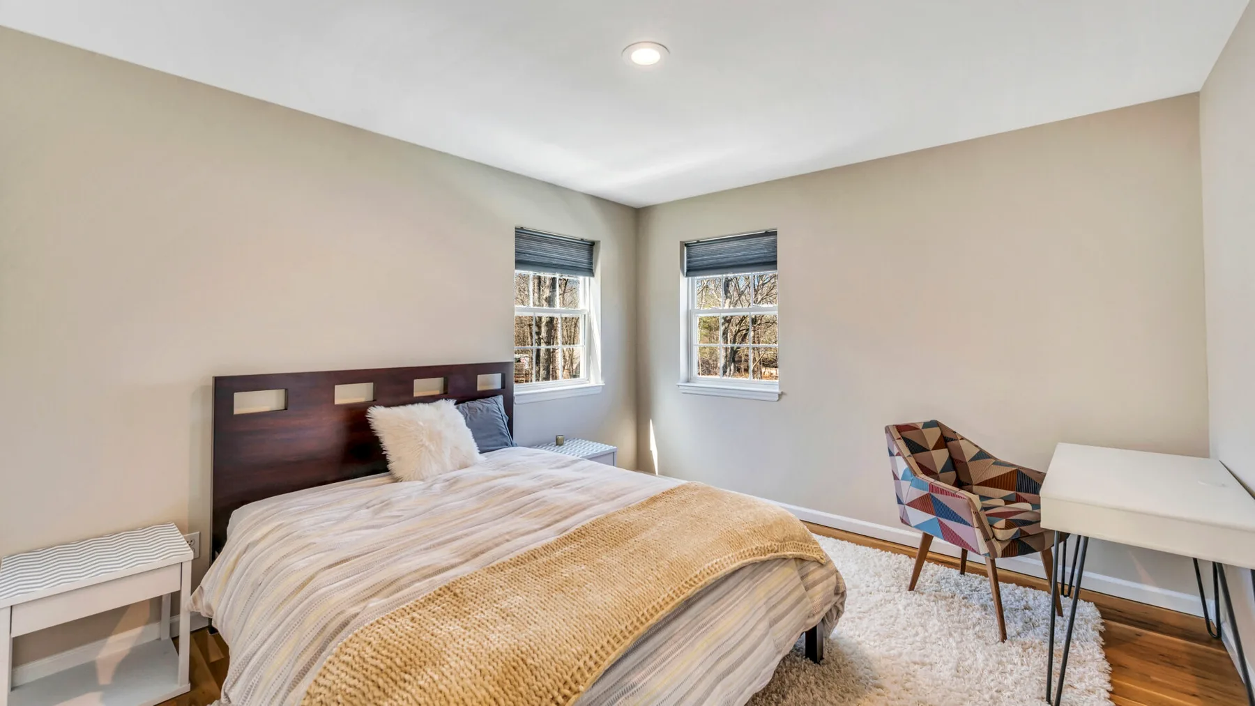 A bright bedroom with a bed, two windows, and a small seating area.