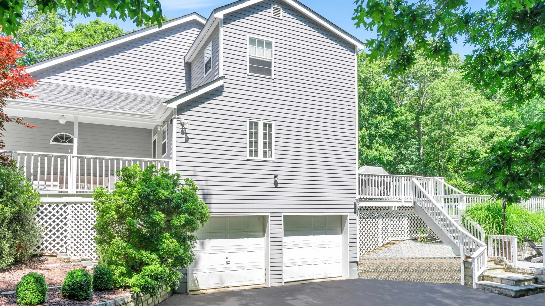 A light-colored two-story house with garage doors, a porch, and an exterior staircase.