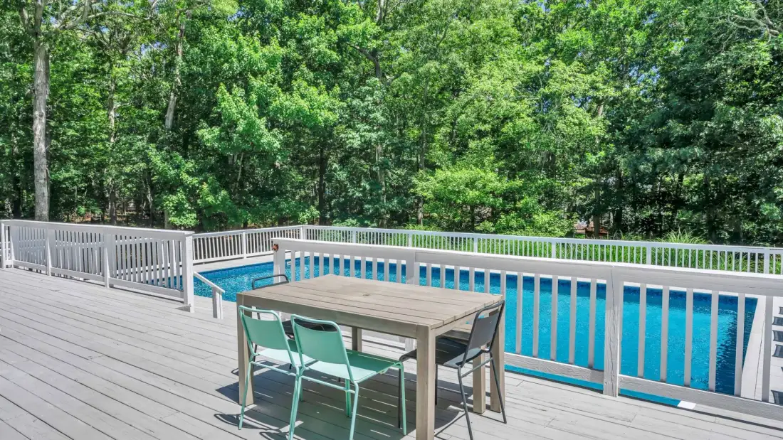 A swimming pool beside a wooden deck with a table and chairs.