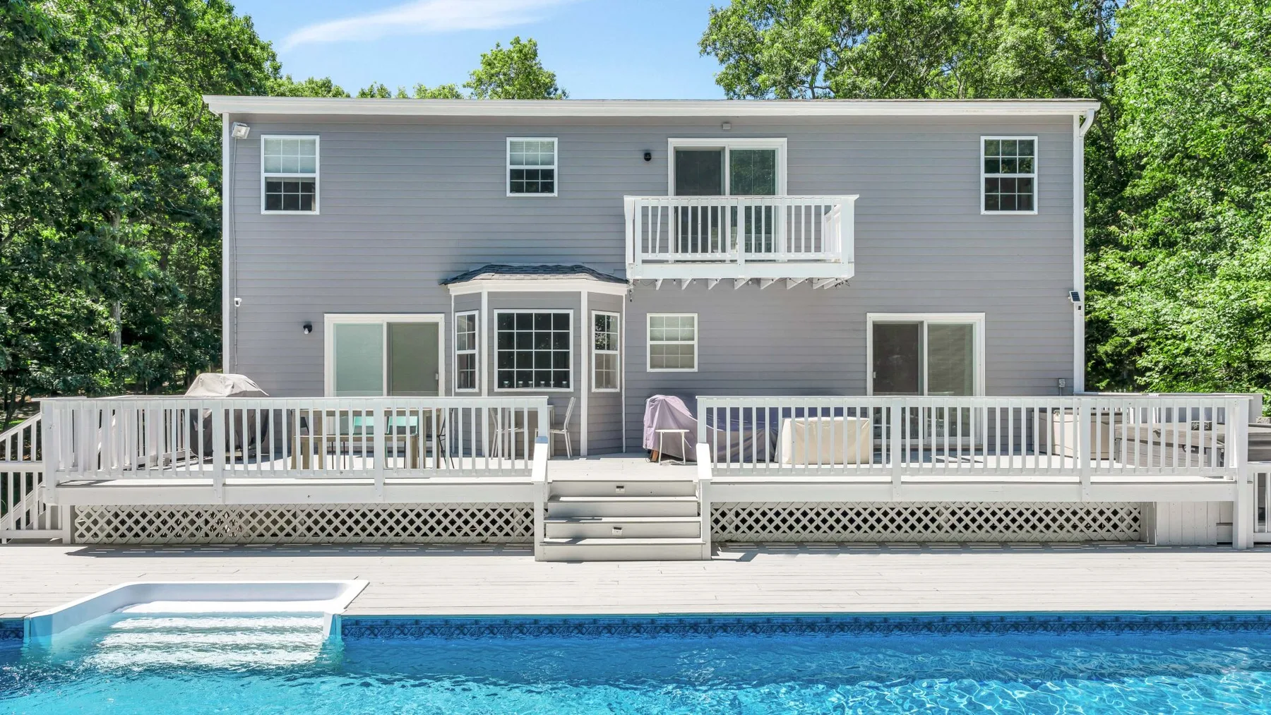 A two-story house with a raised deck overlooks a swimming pool.