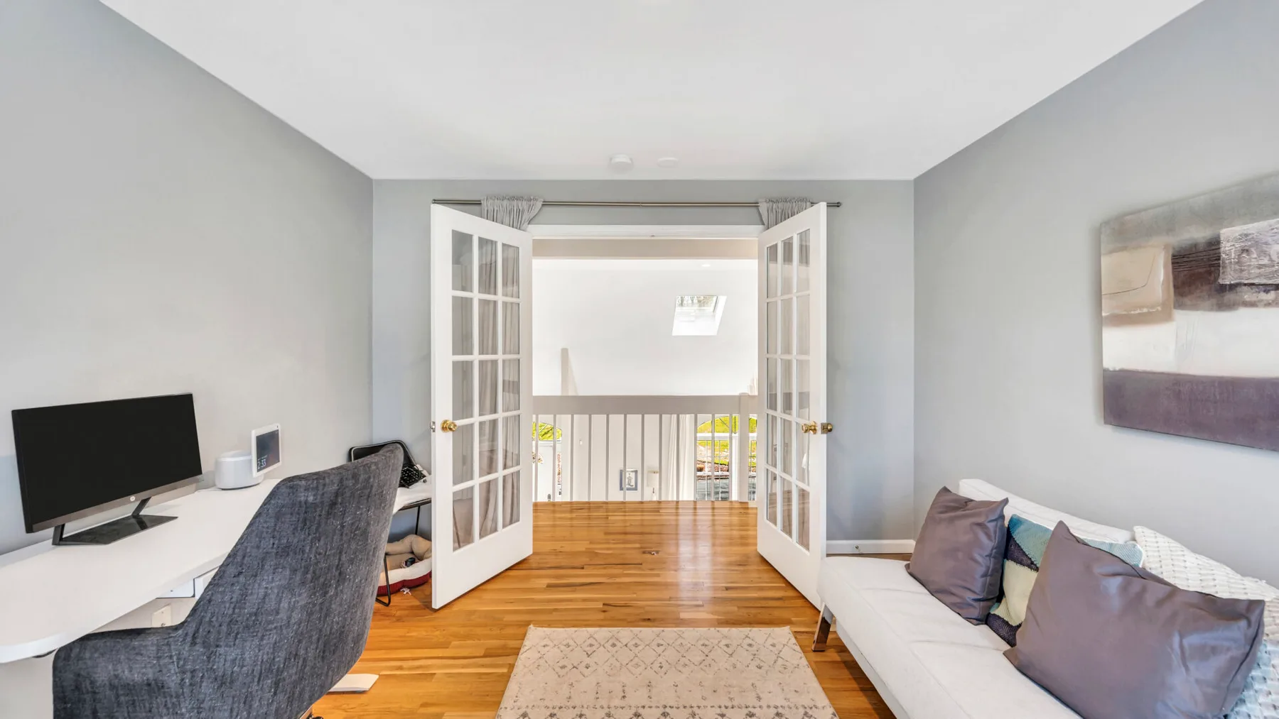 A living room with seating, a desk, and open French doors.