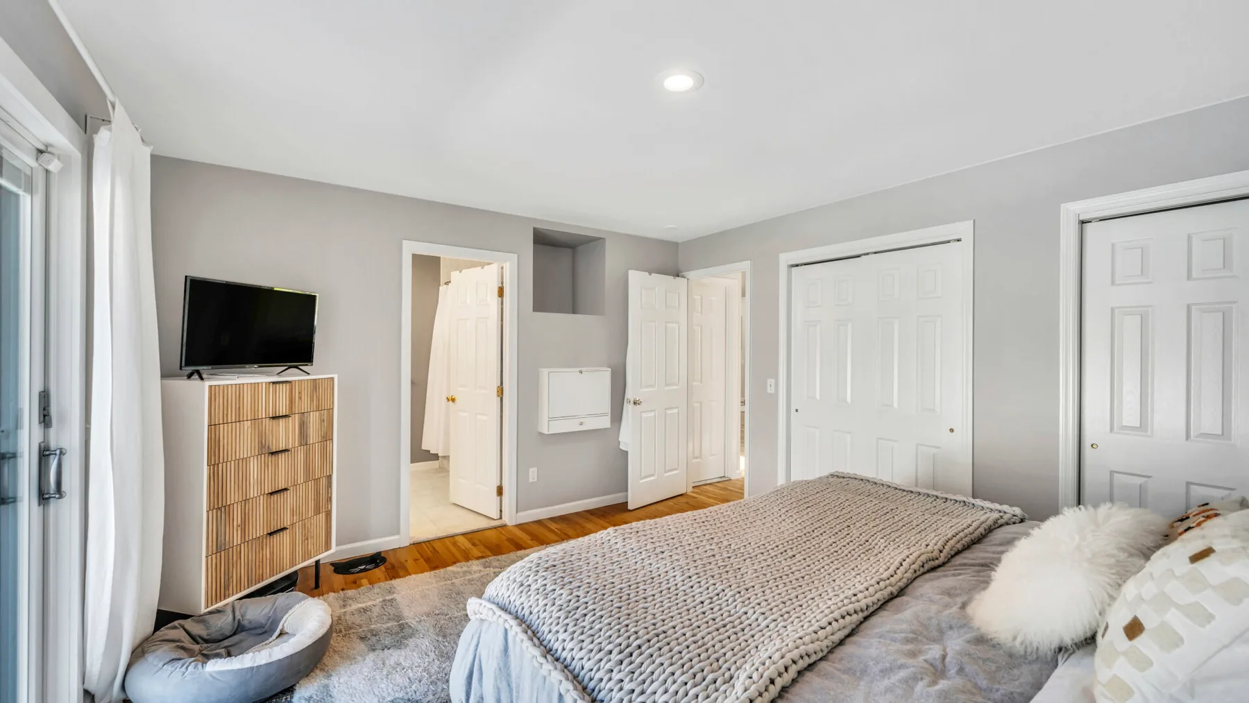 A bedroom with a bed, a television, and several doors.