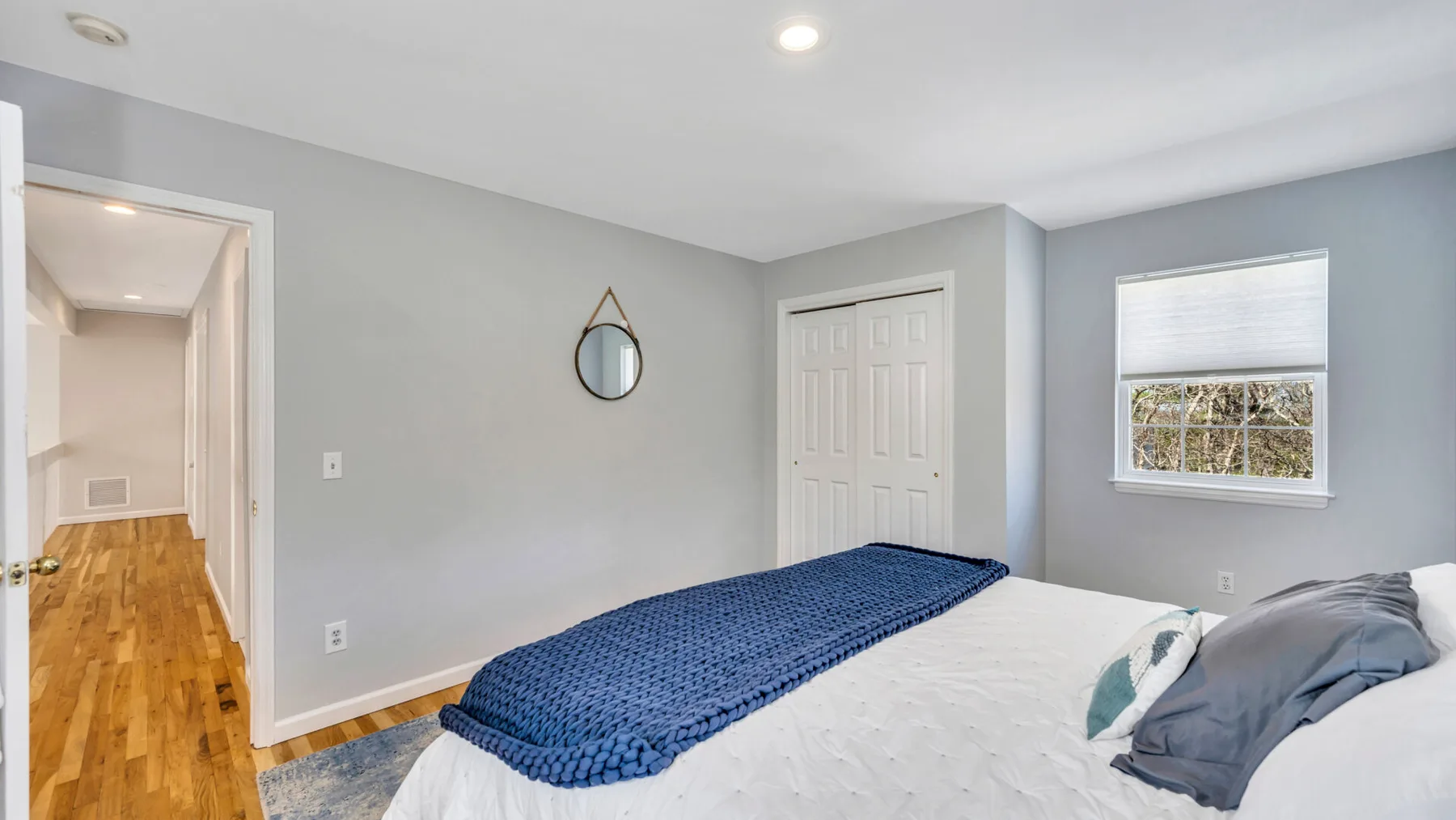 A bedroom with a bed, a window, and a small wall mirror.