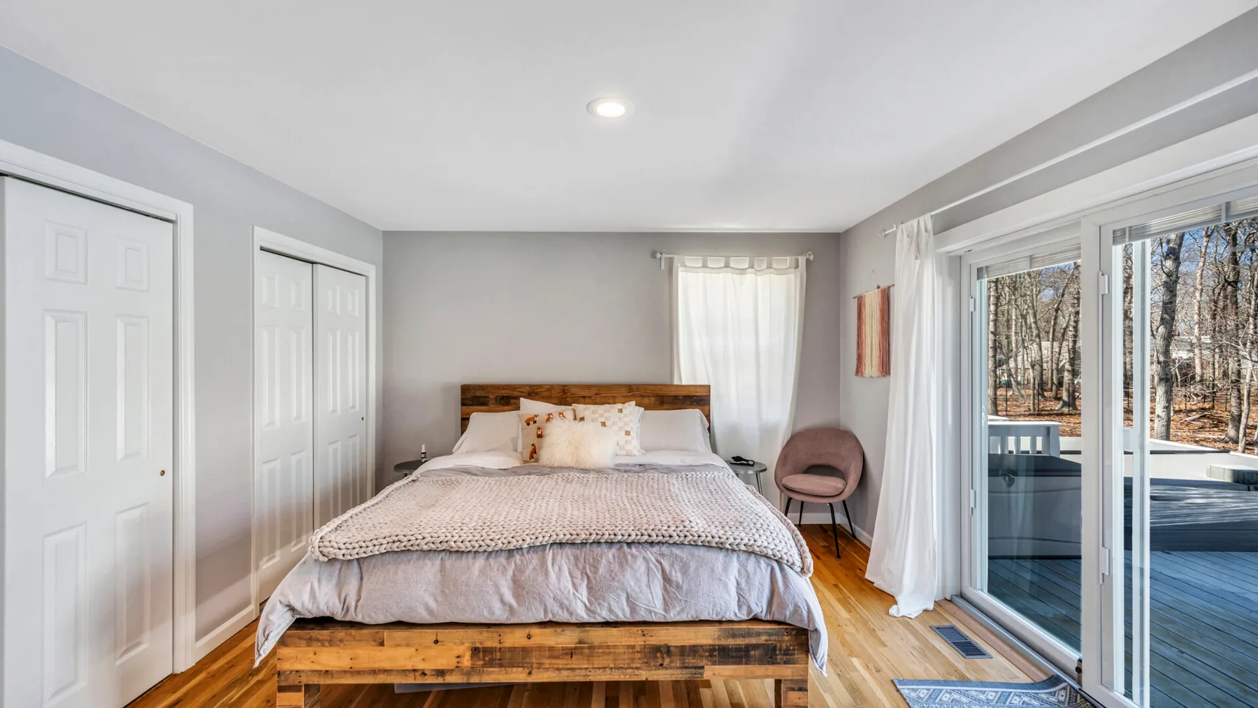 A bright bedroom with a wooden bed and sliding glass doors opening to a deck.