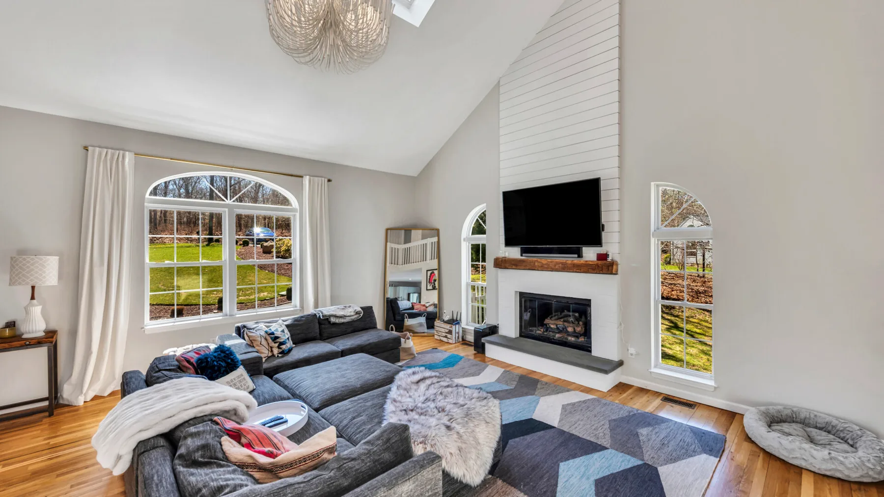Una sala luminosa con asientos grises, una chimenea y ventanas grandes.