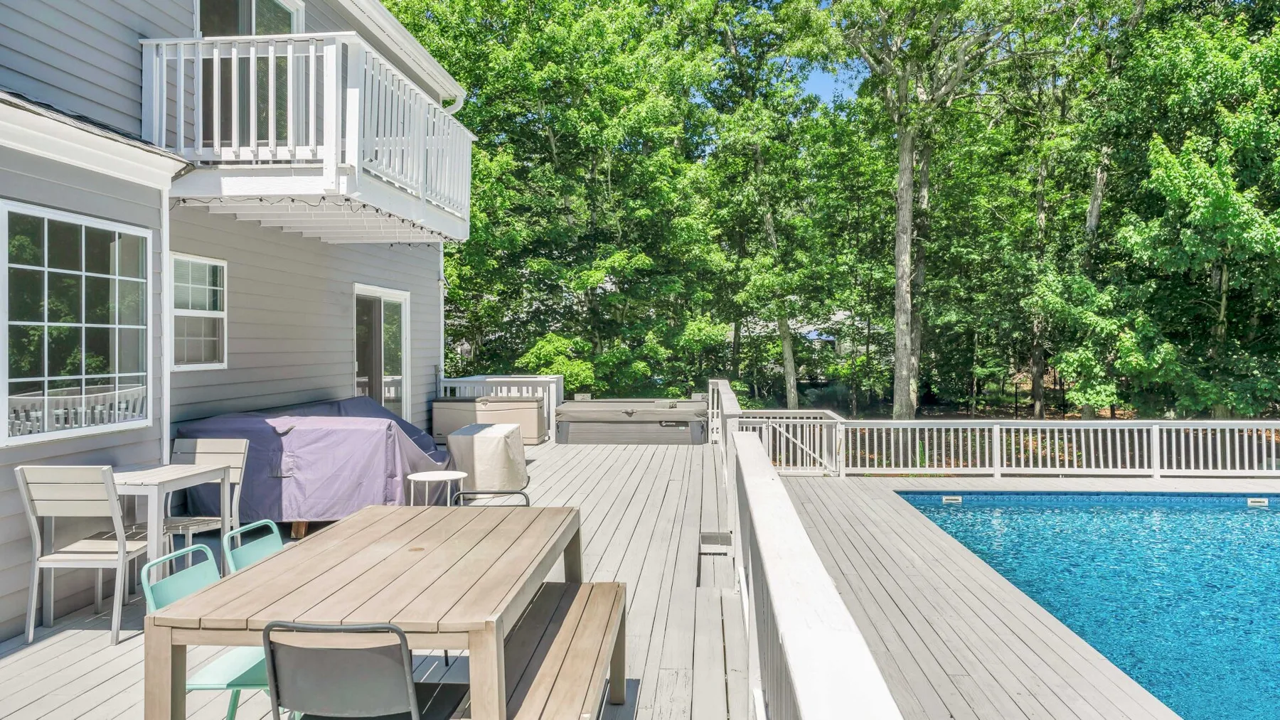 A spacious outdoor deck with a dining table, seating, and a swimming pool beside a house.