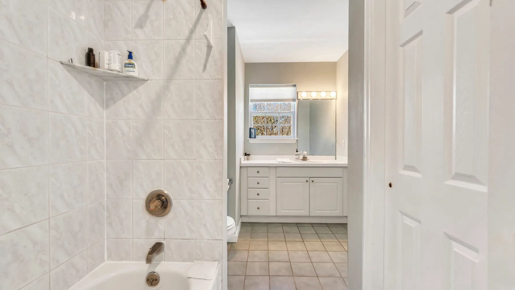 A bathroom with a tiled shower area, vanity, and window.