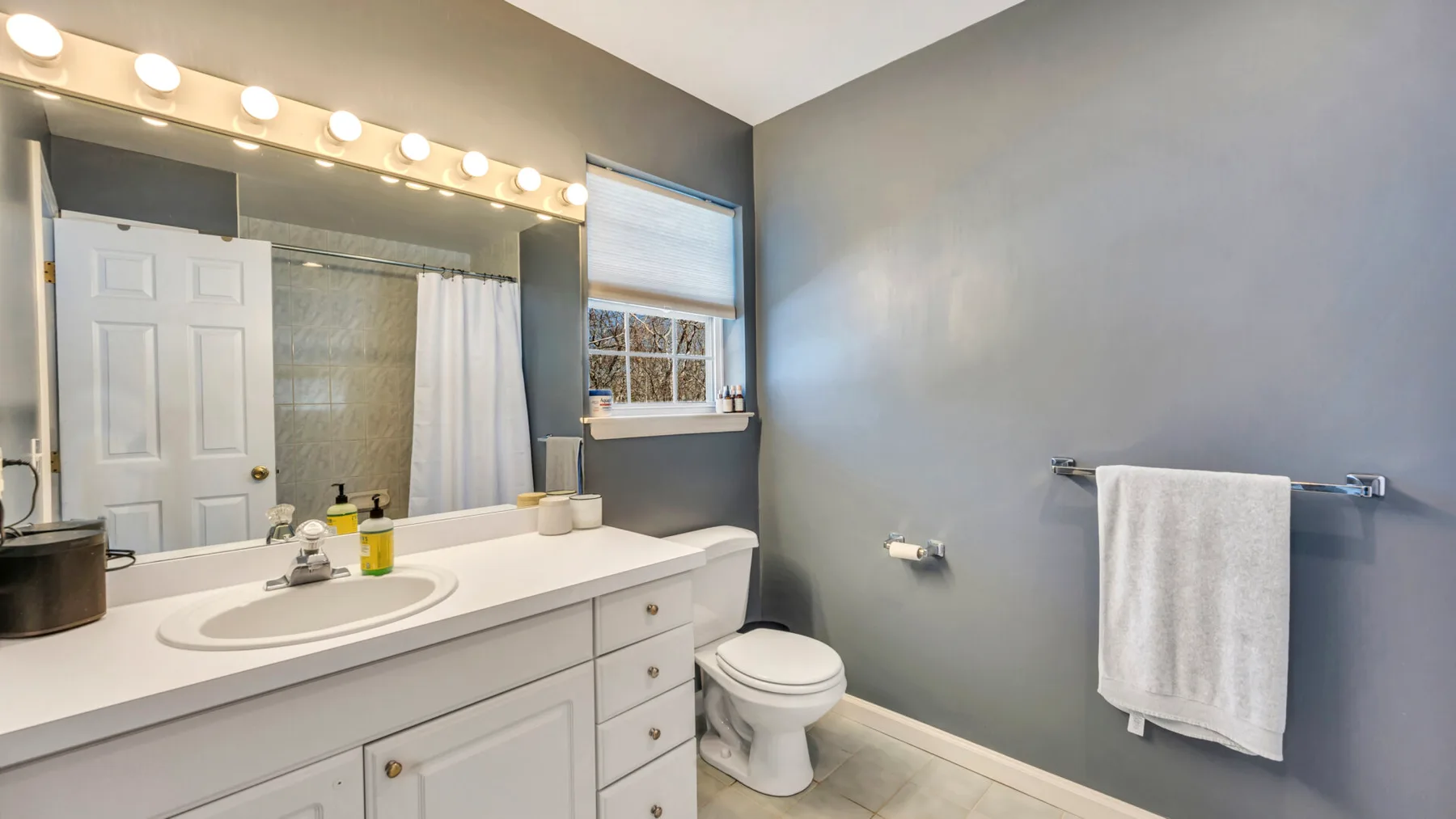 A bathroom vanity and mirror sit beside a toilet and towel rack.
