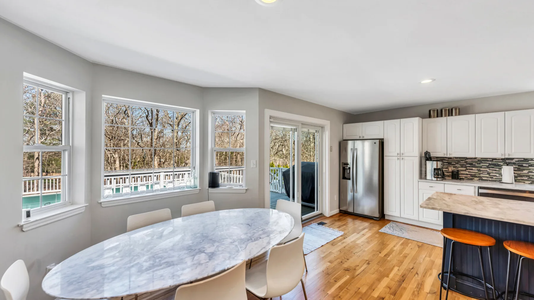 A bright dining and kitchen area with an oval table beside large windows.