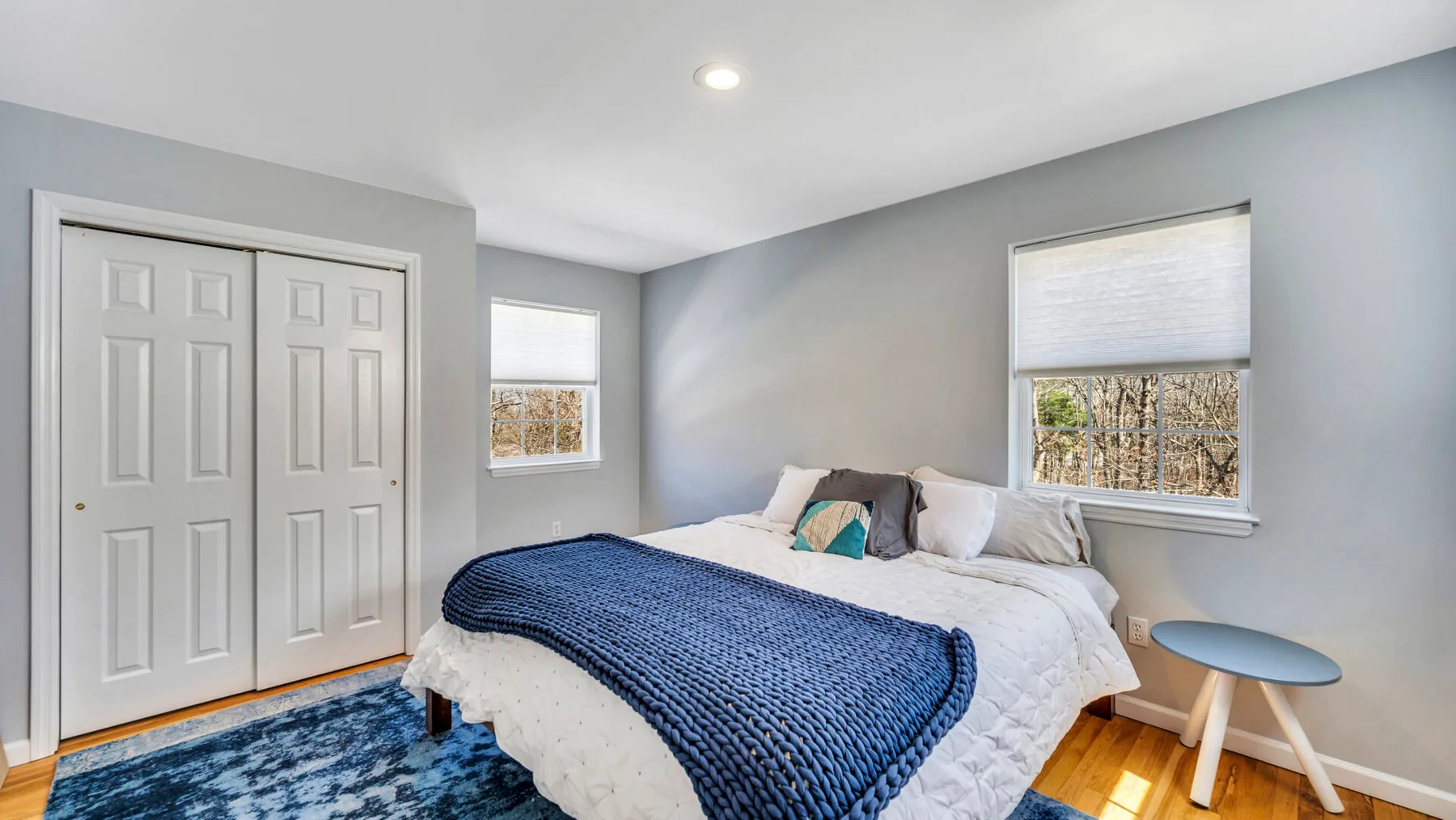 A bedroom with a bed, blue blanket, and windows.