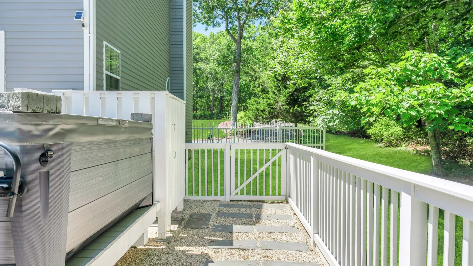 A gated outdoor deck with white railings overlooks a green yard.