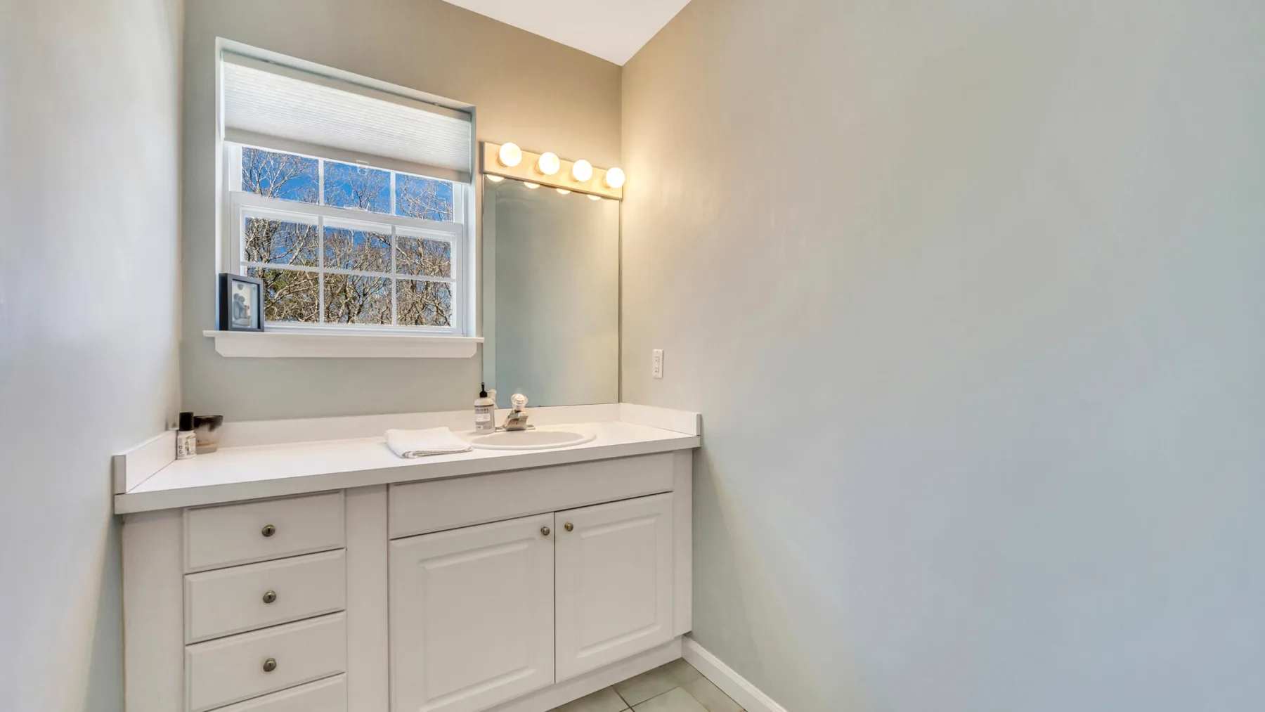 A bathroom vanity with a wide counter, mirror, and window.