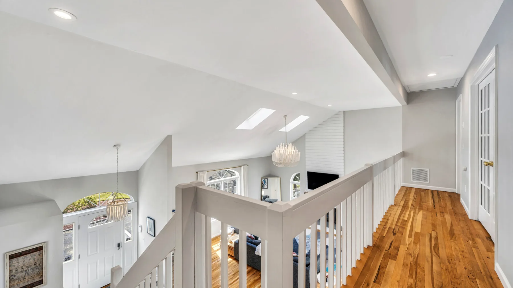 A bright loft landing with a wooden floor and white railing.