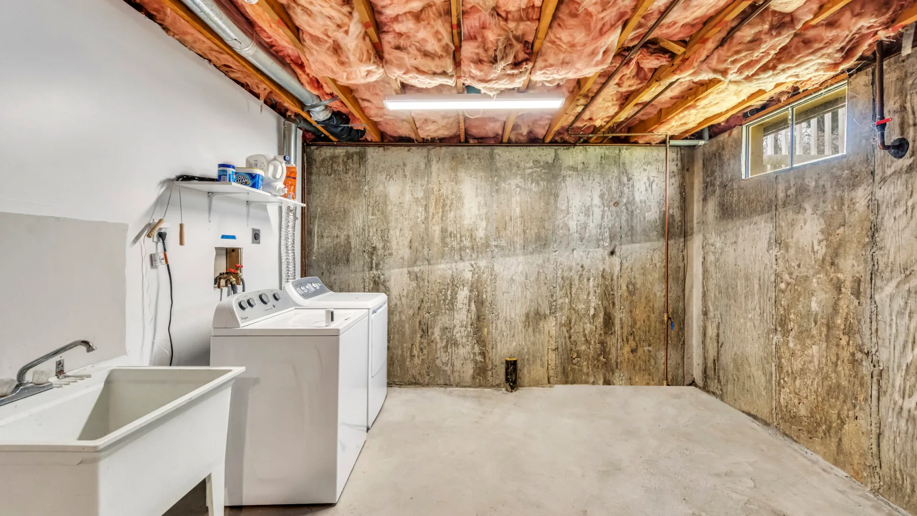 An unfinished basement laundry area with a utility sink and washing machines.