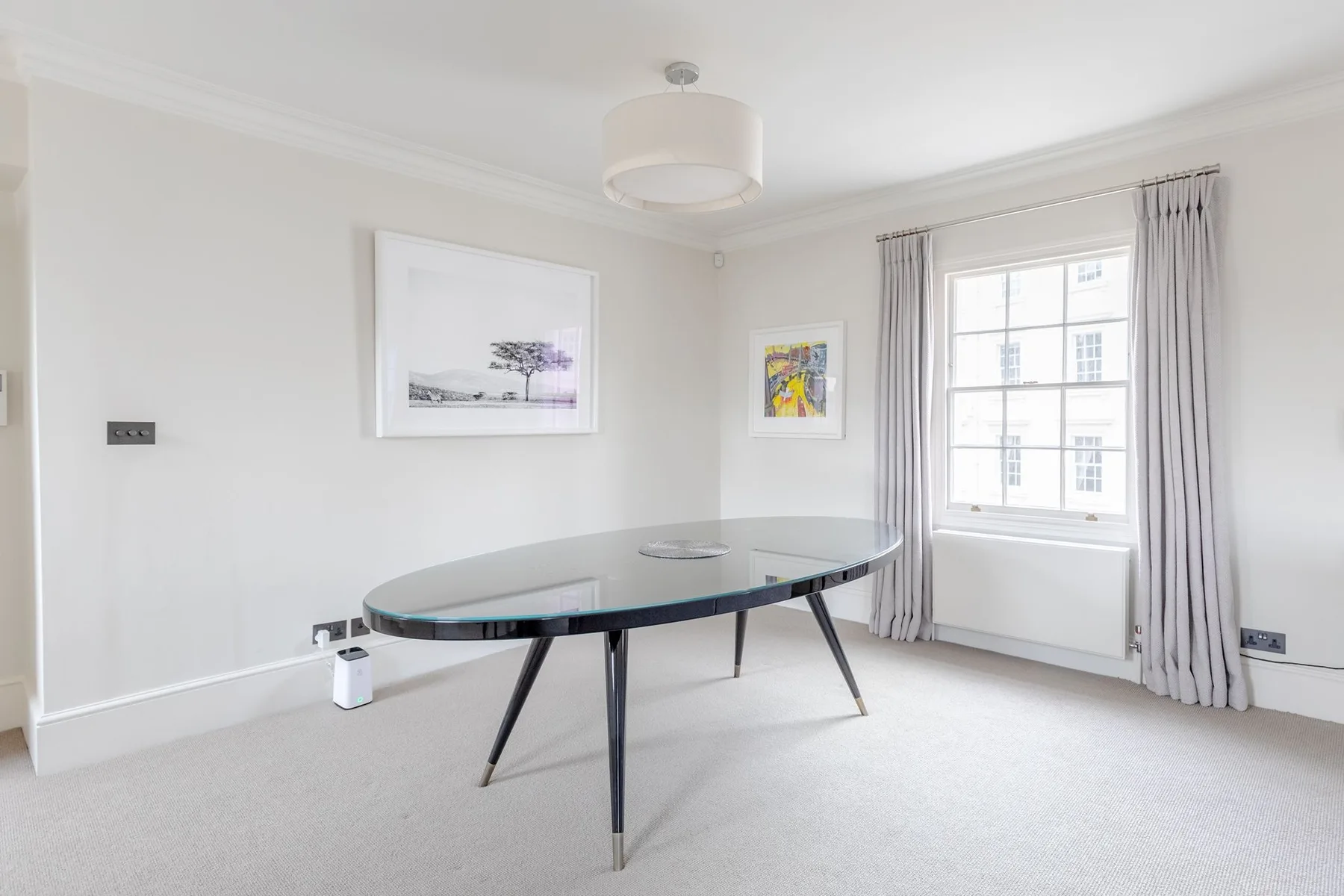 Un comedor luminoso con una mesa, cuadros y una ventana con cortinas.