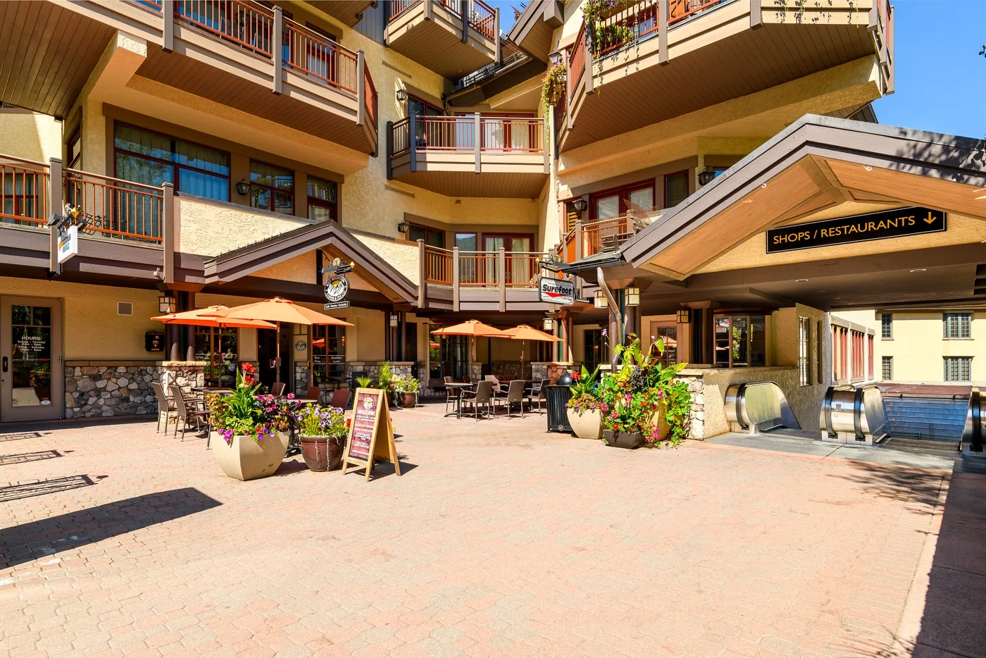 A sunny outdoor courtyard with restaurant seating, umbrellas, and surrounding balconies.