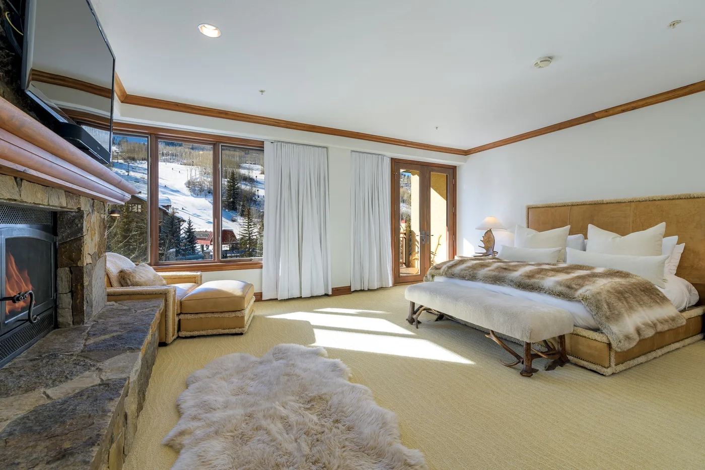 A bright bedroom with a large bed, windows, and a stone fireplace.