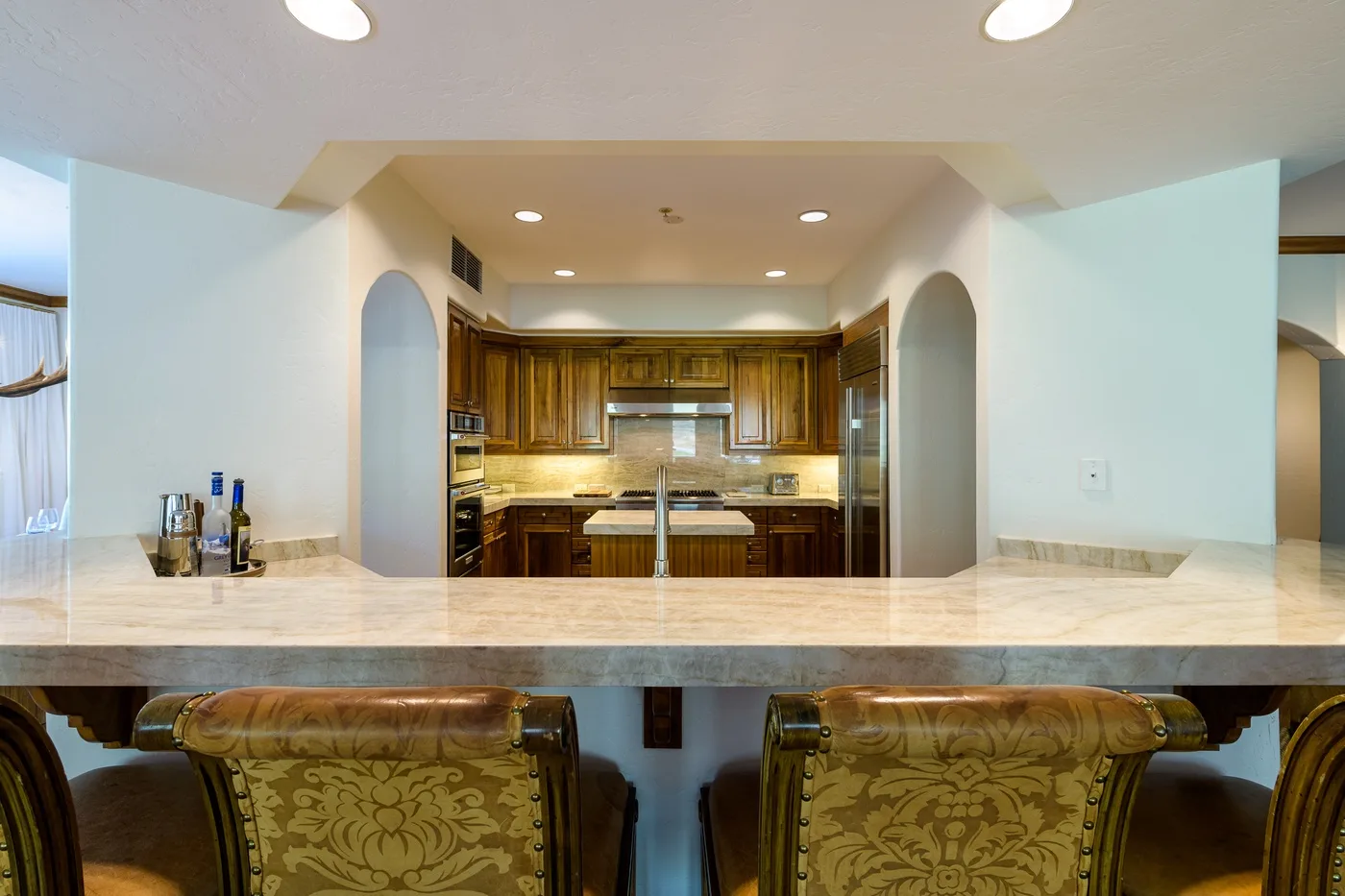 A kitchen with wooden cabinets is visible beyond a wide counter and dining seating.