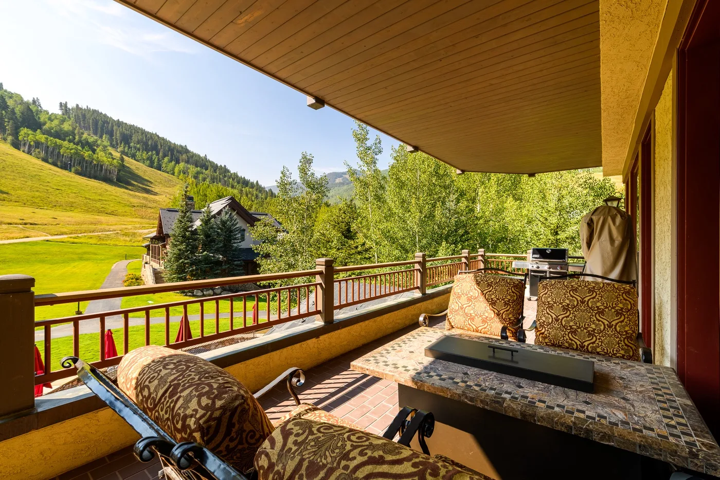 A covered outdoor seating area overlooks a green hillside and nearby buildings.