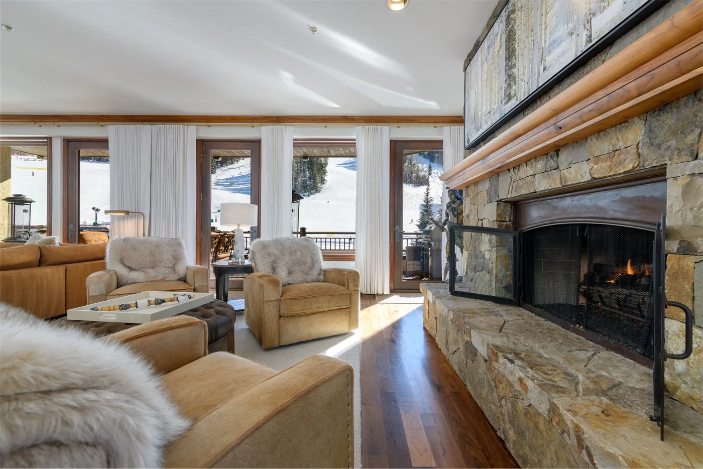 A living room with seating beside a stone fireplace and large windows.