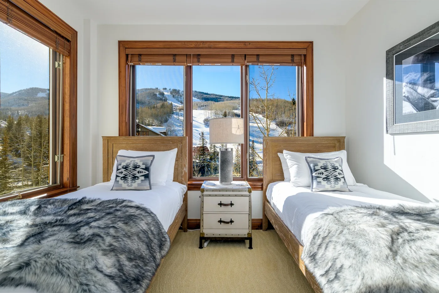 A bright bedroom with two single beds beside large windows overlooking a snowy landscape.