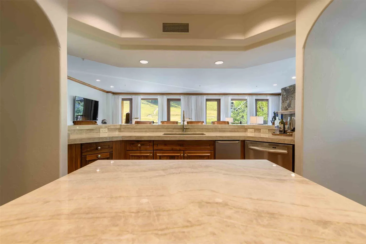 A kitchen with a broad countertop and wooden cabinets beneath a row of windows.