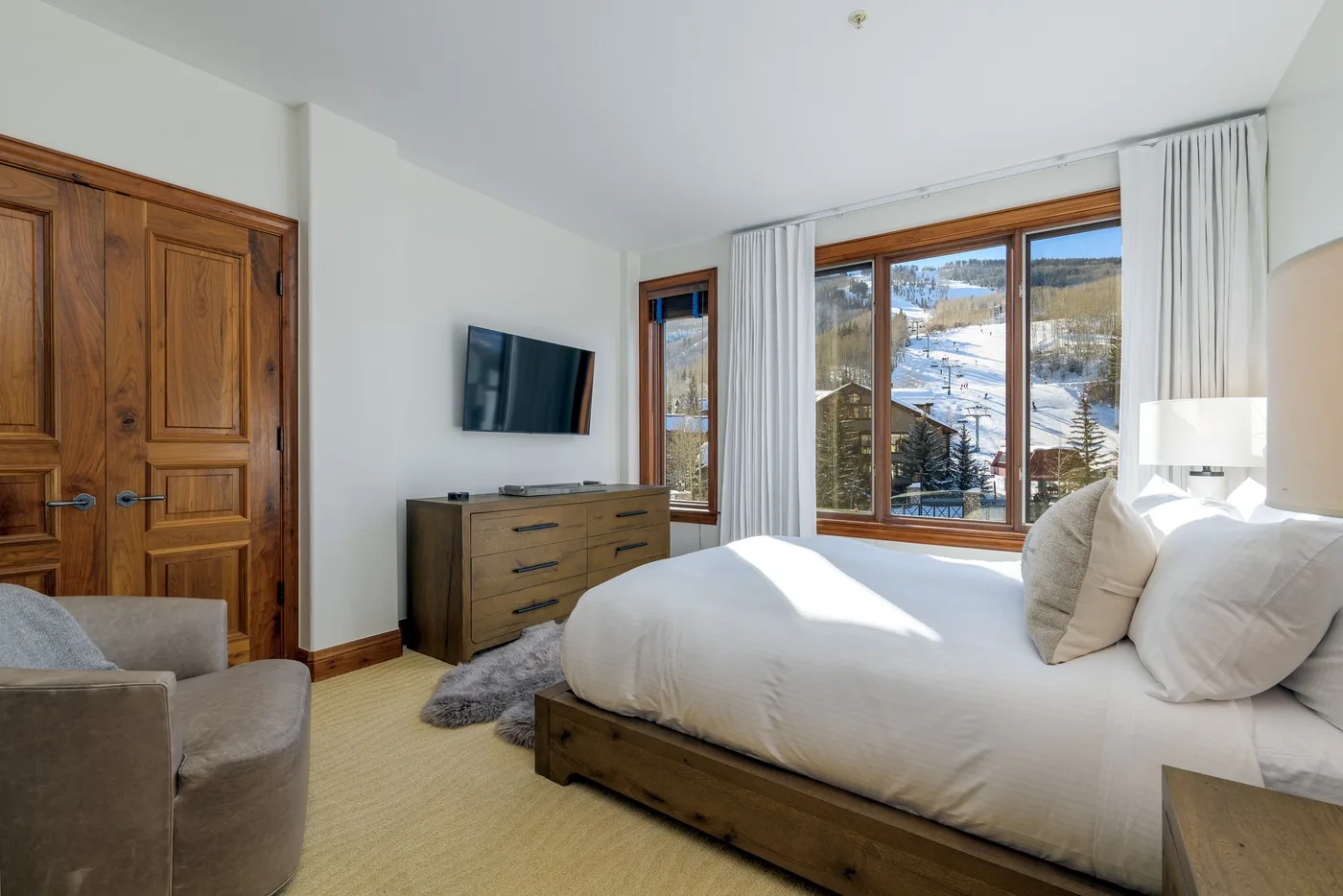 A bright bedroom with a large bed, wooden furnishings, and a mountain view through the window.