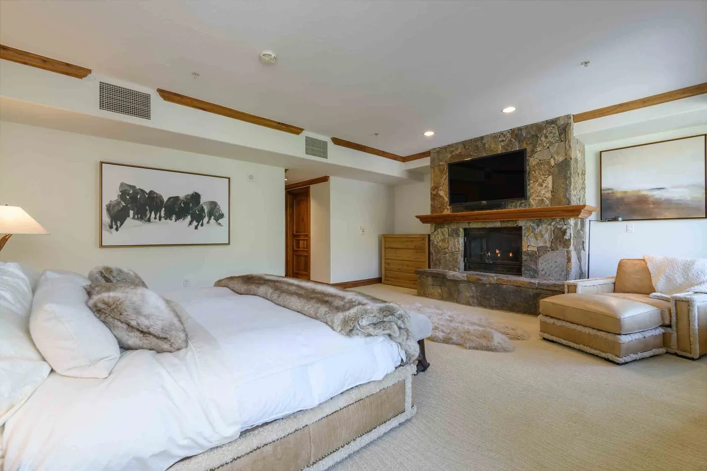 A spacious bedroom with a large bed and a stone fireplace beneath a television.