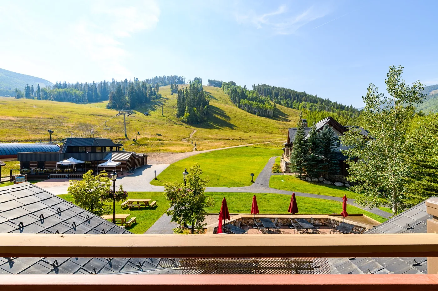 A hillside resort overlooks green slopes, scattered trees, and a winding path.