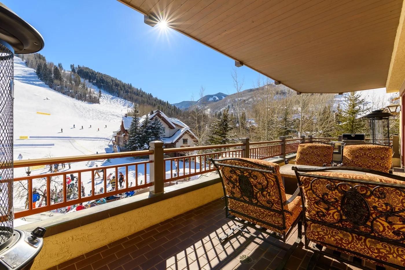 A sunny balcony overlooks a snowy ski slope and mountain scenery.