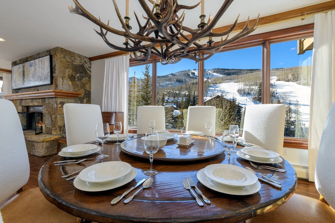 A dining area with a set table beside large windows overlooking a snowy landscape.
