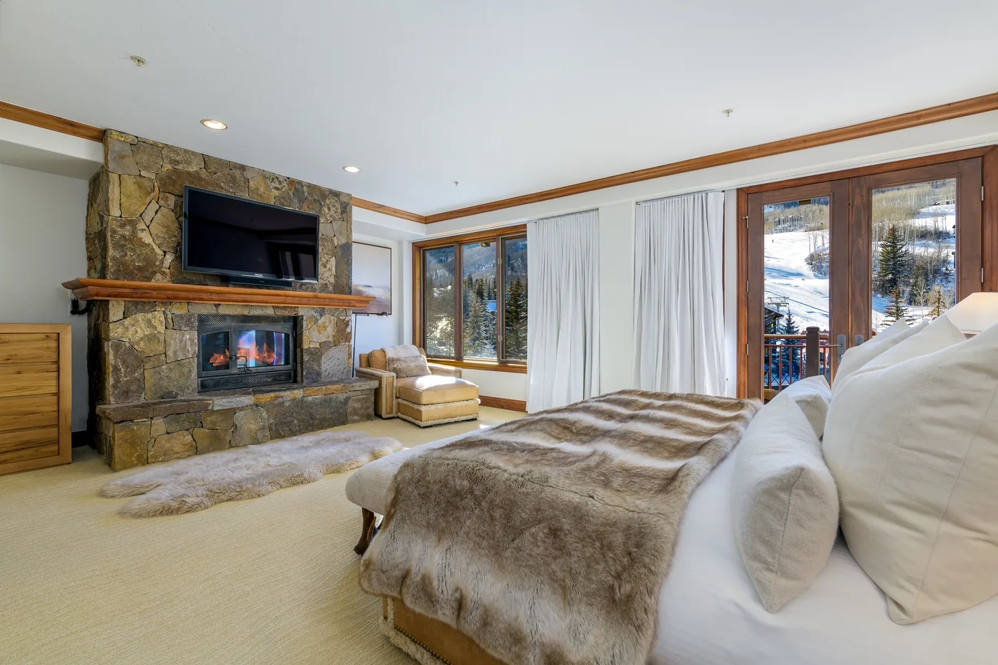 A bedroom with a bed facing a stone fireplace and television.