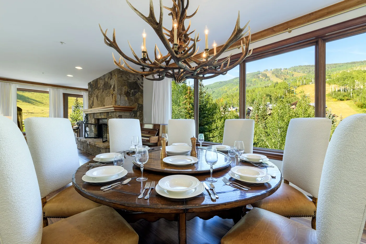 A dining room with a set table beside large windows overlooking green hills.