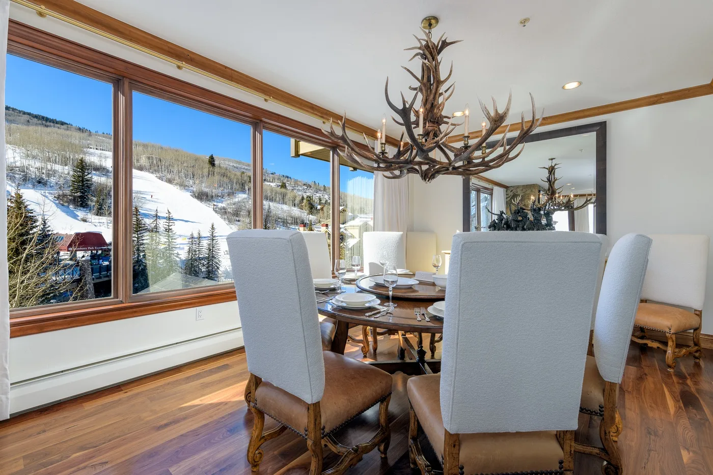 A dining room with upholstered seating around a table beside large windows overlooking a snowy landscape.
