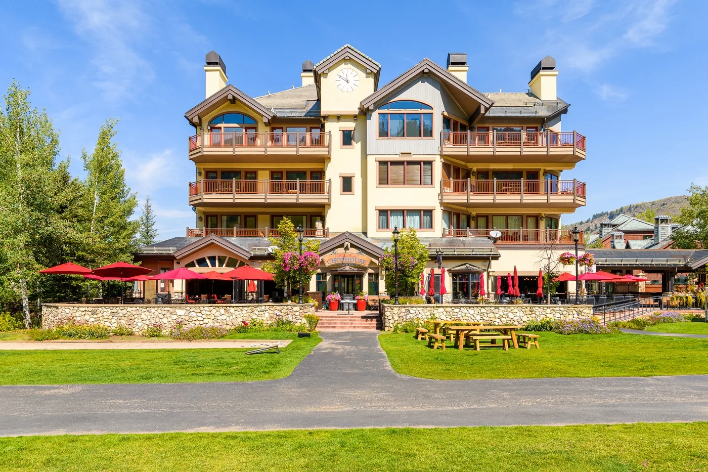 A multi-story lodge stands behind a lawn, with red patio umbrellas along the front.