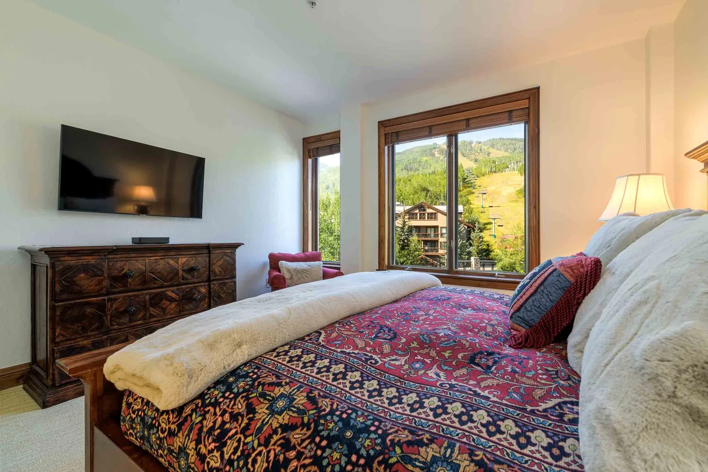 A bedroom with a patterned bedspread and large windows overlooking a green hillside.